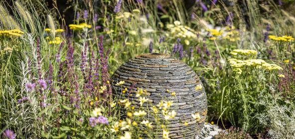 500mm Rustic Slate Watersphere nestled in a raised bed with yellow and purple flowers. Used in a Gold medal award winning Garden at Tatton Park Flower Show 2023.
