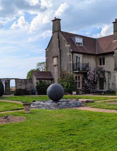 Slate-walled pond with a 1.2m slate ball Watersphere at the center, set at a crossroads of a pebbled pathway in a manor house garden with expansive green lawns.