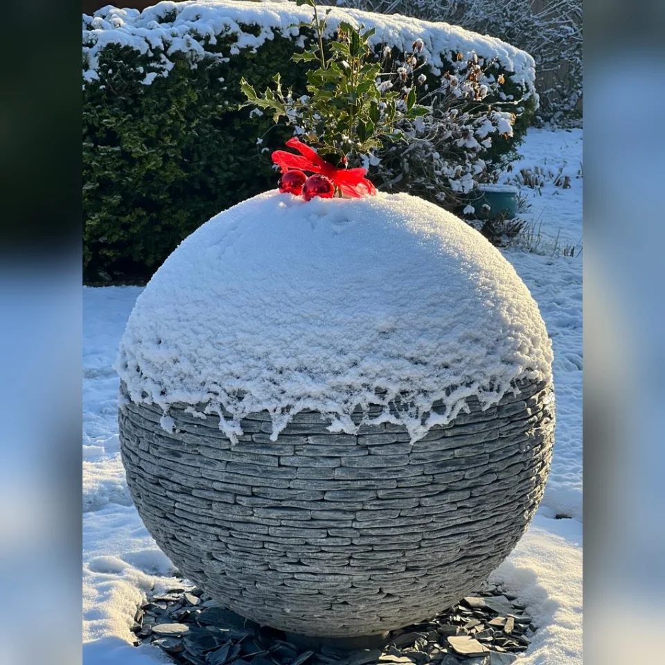 800mm Grey Watersphere™ covered in snow during the Christmas period 2022. The customer has dressed the sphere with some holly, baubles and ribbons to make it look like a Christmas pudding!