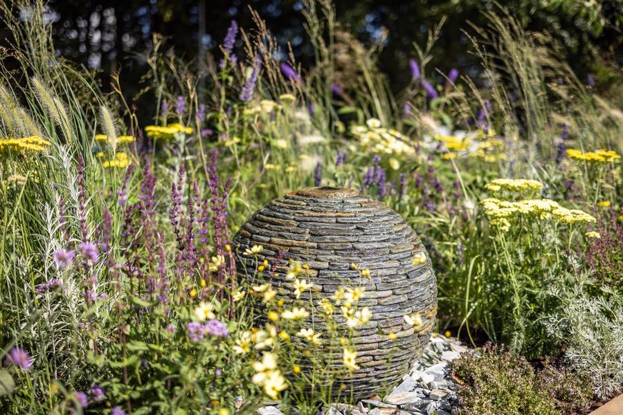 500mm Rustic Slate Watersphere nestled in a raised bed with yellow and purple flowers. Used in a Gold medal award winning Garden at Tatton Park Flower Show 2023.