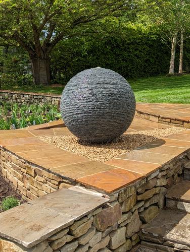 Jeremy Hastings 1m Large grey slate ball water feature, at the top of a steep flower bed, with carefully designed paving to create the splash zone from the water.