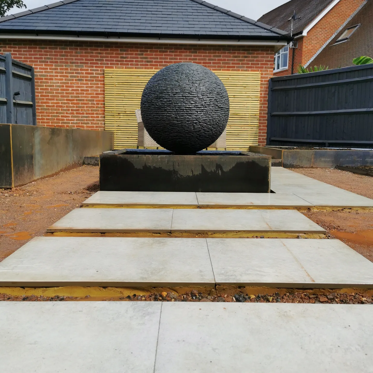 Jeremy Hastings 1m Large grey slate ball water feature, set on a raised square Corten steel framed pond. Surrey.