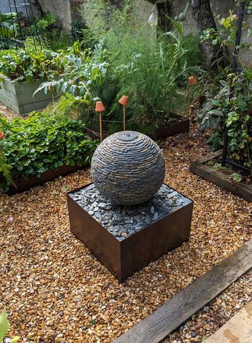 Jeremy Hastings 500mm extra small rustic slate ball water feature, on a square Corten steel base. Installed in a beautiful garden in Portcatho, Cornwall which has matching steel edging on the vegetable patches.