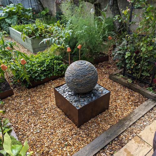Jeremy Hastings 500mm extra small rustic slate ball water feature, on a square Corten steel base. Installed in a beautiful garden in Portcatho, Cornwall which has matching steel edging on the vegetable patches.