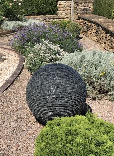 Jeremy Hastings 650mm small grey slate ball water feature, gravel lined flower bed, Somerset.