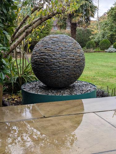 Jeremy Hastings 650mm small rustic slate ball water feature, in a flower bed