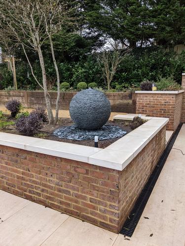 Jeremy Hastings 800mm grey slate ball water feature set in a raised brick flower bed.