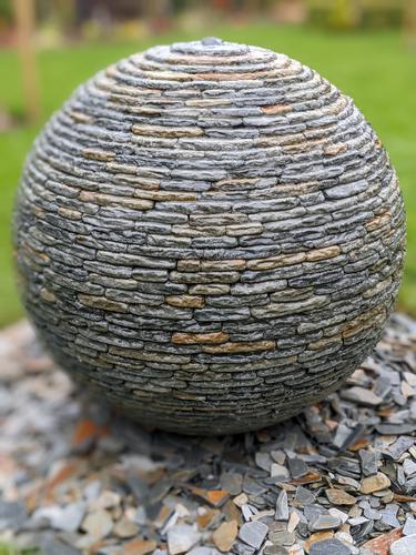 Jeremy Hastings 800mm rustic slate ball water feature installed in a lawn, Horsham