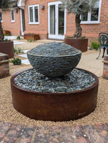 Jeremy Hastings bespoke water feature; rustic slate over-flowing semi sphere on a Corten steel base.