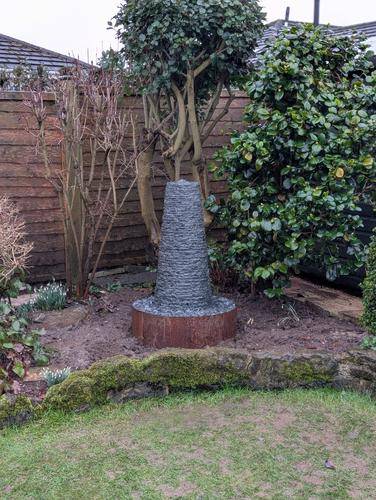 Jeremy Hastings Cornish chimney water feature in a corner flower bed of a small garden