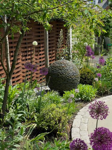 800mm (medium) Rustic slate Watersphere™ set in the flowerbed against a Corten steel fence, surrounded by beautiful Aliums.
